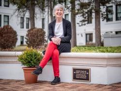 Lise Green sitting on a stone bench. Her name plaque is attached to the bench.